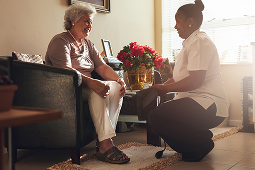 Elderly woman in chair smiling and talking with caregiver