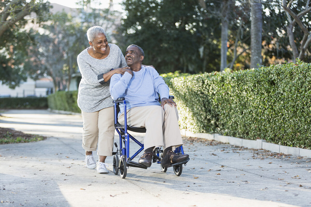 Caregiver lauging with client as she pushes him in wheelchair