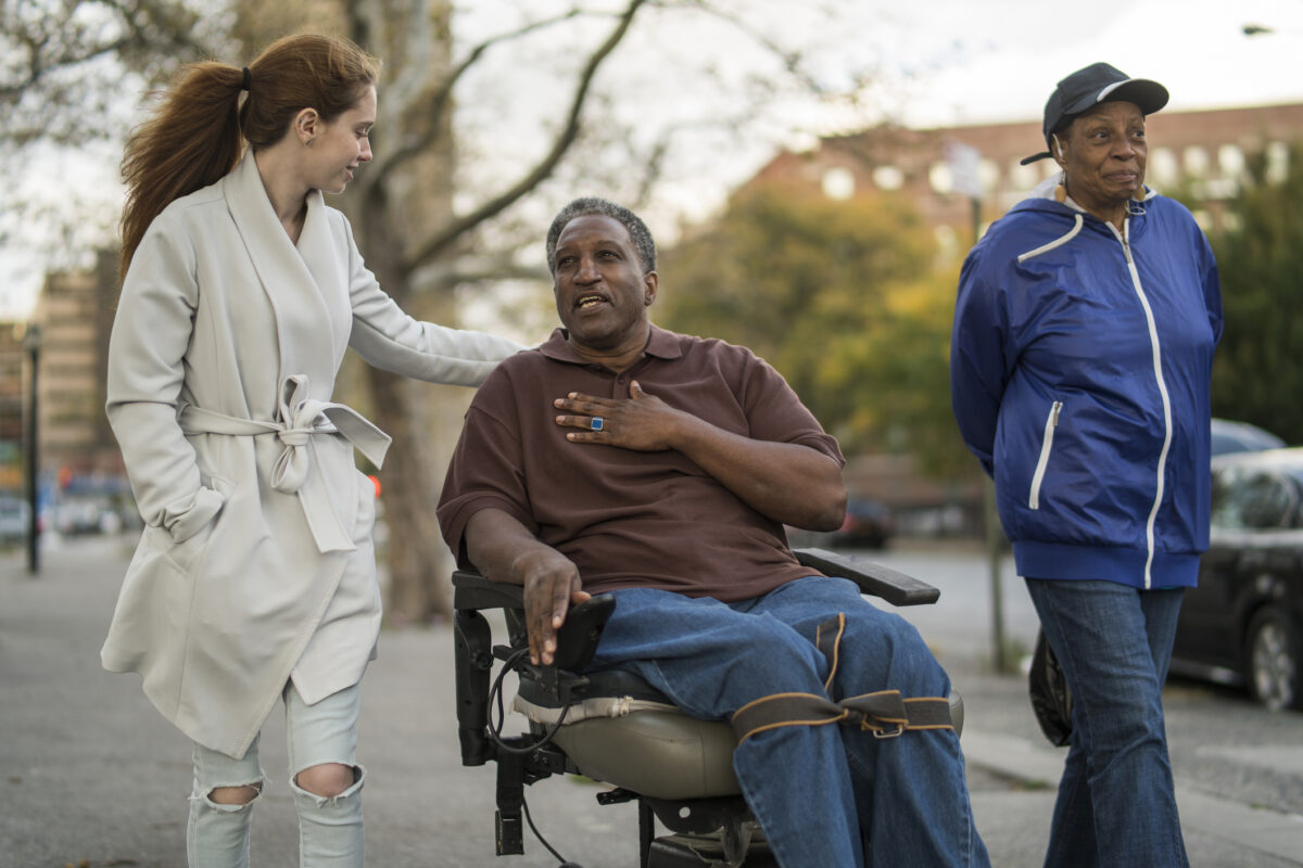 Man in wheelchair explaining something to caregiver while friend walks alongside