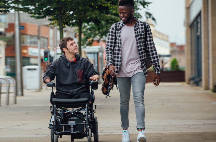 Caregiver walking with young man in wheelchair downtown