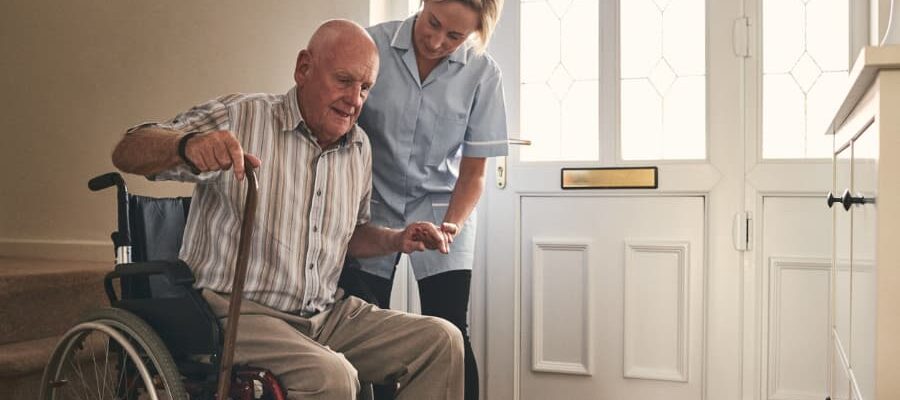 Caretaker helping disabled senior man to get up from wheelchair