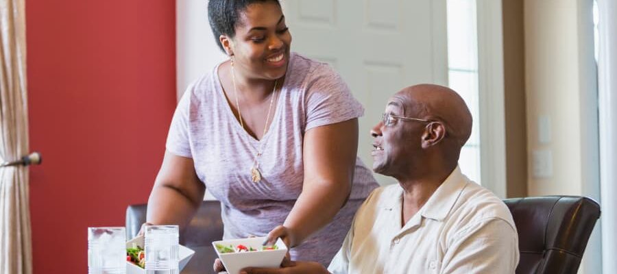 Caregiver serves a bowl of food to a person seated at a table