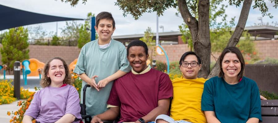 Diverse group of people living with disabilities sits on a park bench