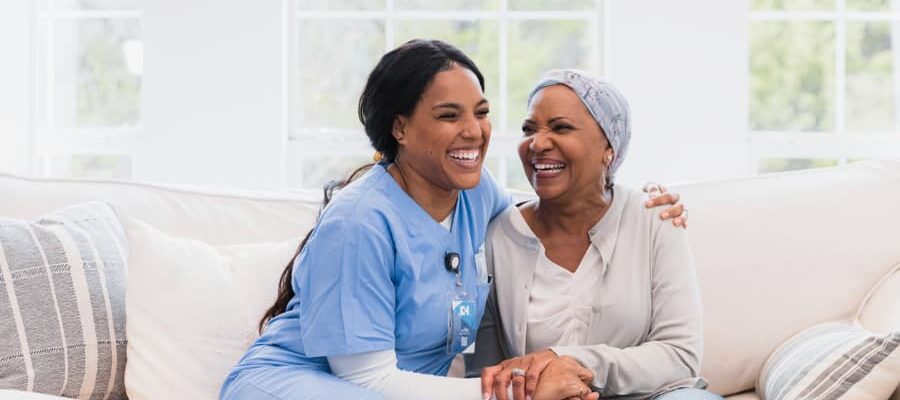 Caregiver and senior adult with cancer embrace and laugh during home visit