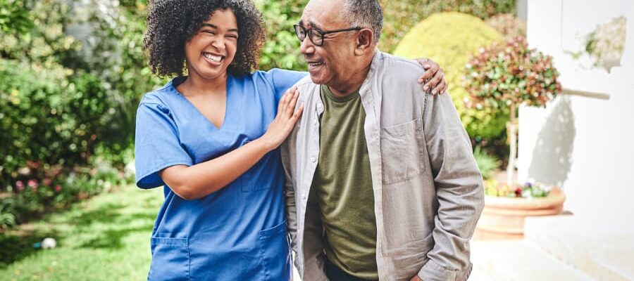 Young nurse smiling with senior male patient outside