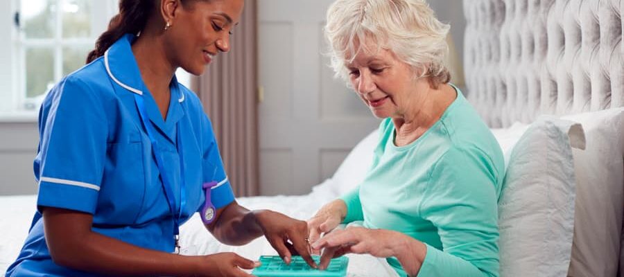 Female care worker in uniform helping senior at home in bed with medication