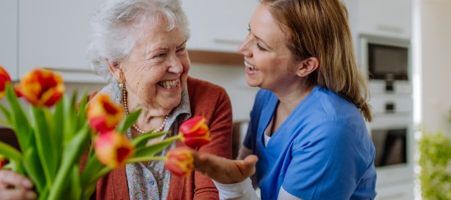 Caregiver laughing with patient as they put flowers into a vase